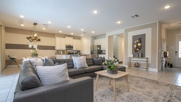 Un salon moderne avec un canapé d’angle gris, une table basse et un coin repas comprenant une table et des chaises blanches.