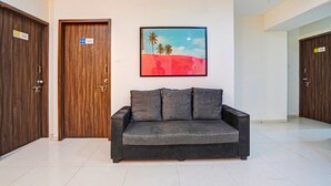 A lobby with a grey sofa, wooden doors, and a framed picture on the wall. - Classic With Balcony I- Siri Lodge (Pune)