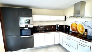 A modern kitchen with dark cabinets, a microwave, a stove, and a coffee maker. - Neiz Vran House Facing the Sea (Kerlouan)