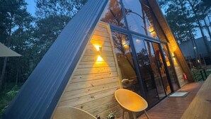 A modern, triangular wooden structure with glass walls, two wicker chairs, and a wooden deck. - Alpine Villa | Mountain| Fire pit| Heated Jacuzzi (Jarabacoa)