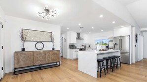 A modern kitchen with a central island, bar stools, and a decorative wall piece. - Entertaining Estate: Pickleball, B-ball & Golf! (Phoenix)