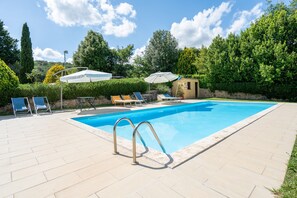 Ein Pool mit Liegestühlen und Sonnenschirmen, umgeben von Grünflächen und einer Steinmauer.