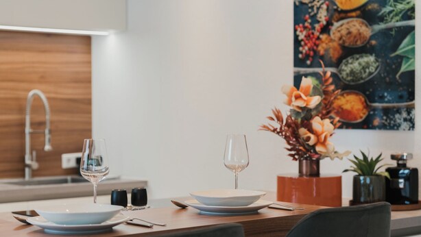 A modern kitchen with a dining table set for two, featuring two wine glasses, a vase with flowers, and a painting on the wall. - Modern City Center Apartment at Mirabell Palace (Salzburg Stadt)