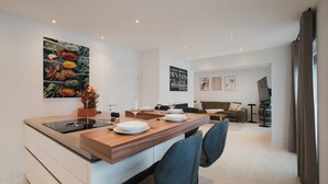 A modern kitchen with a central island, dining area with chairs, a sofa, and a TV. - Modern City Center Apartment at Mirabell Palace (Salzburg Stadt)