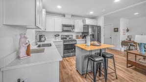 Una cucina moderna con mobili bianchi, elettrodomestici in acciaio inossidabile, un'isola in legno e un'area salotto con sgabelli.