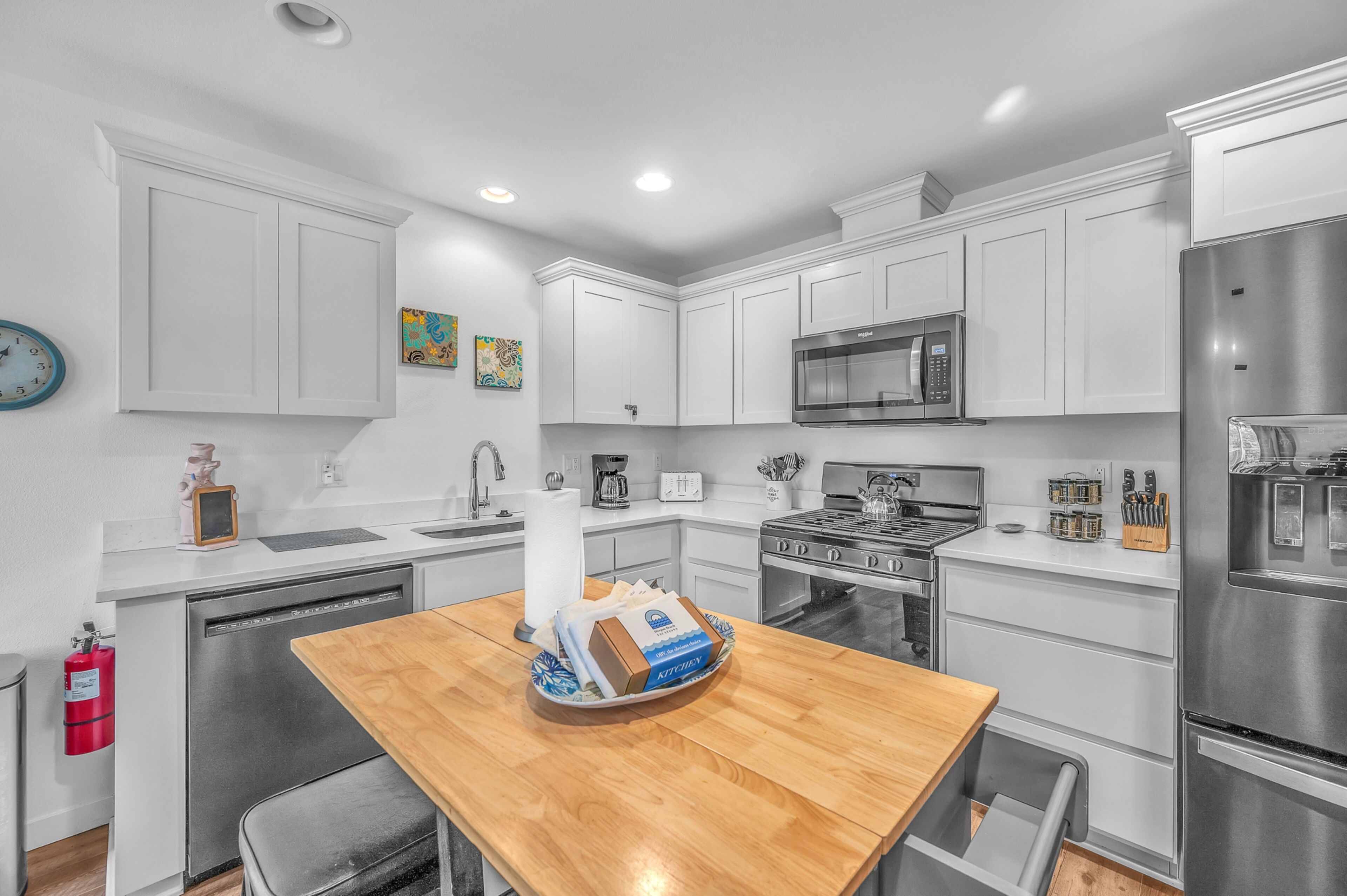 A modern kitchen with white cabinetry, stainless steel appliances, a wooden dining table, and a fire extinguisher.