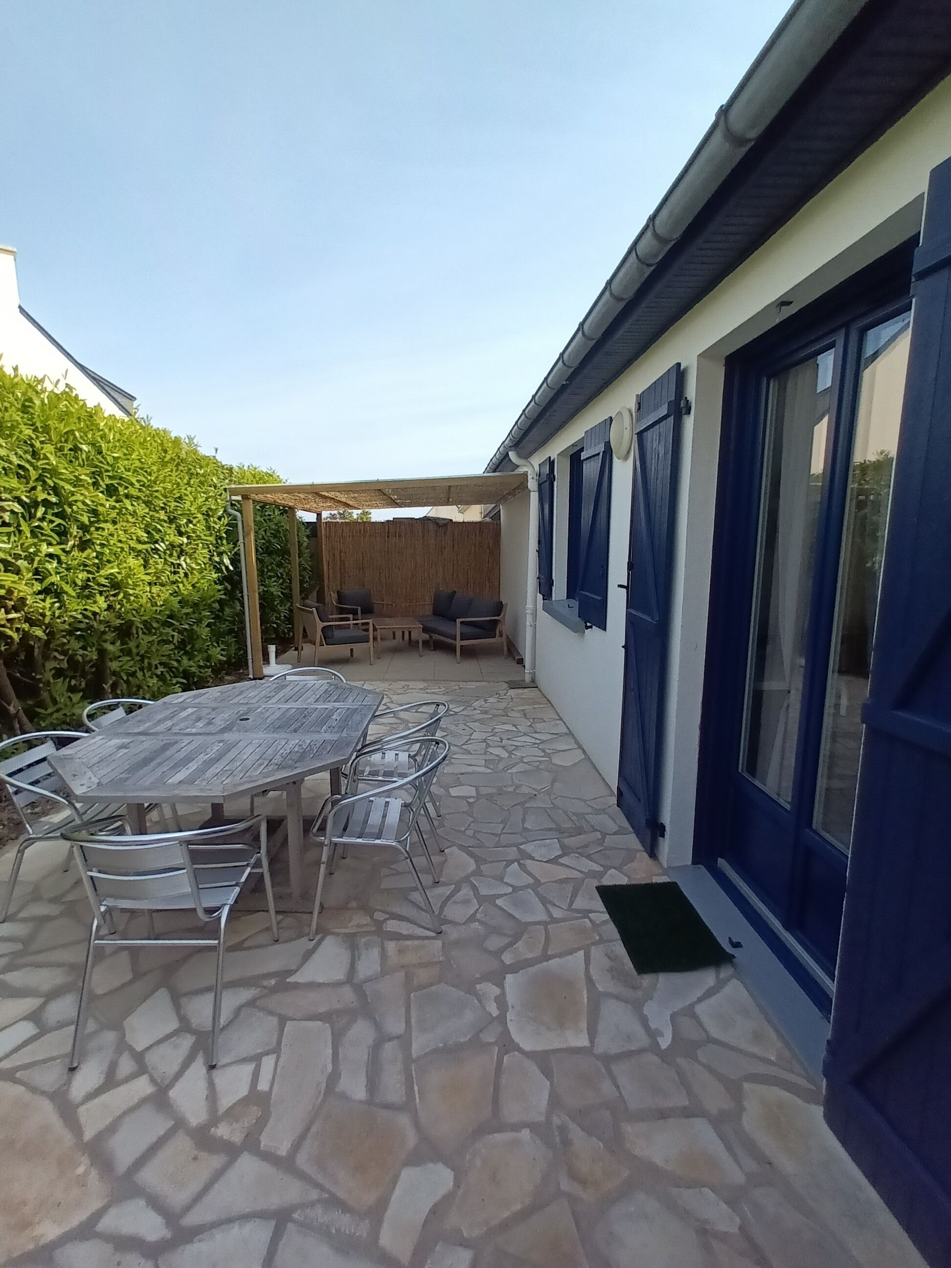 Eine Terrasse mit Steinboden, einem Holztisch und Stühlen, sowie einem überdachten Sitzbereich.