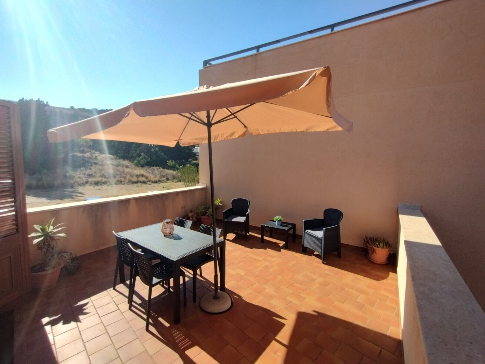 Un patio exterior con mesa y sillas, un paraguas grande y plantas en macetas.