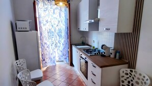 A compact kitchen with a gas stove, white cabinets, and a patterned curtain. - Apartment 'Casa Ariele' with Mountain View, Private Terrace and Air Conditioning (San Vito Lo Capo)