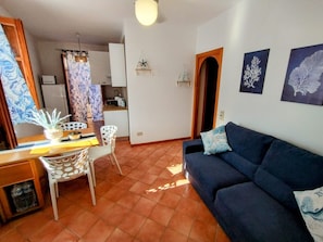 A living room with a sofa, a dining table with chairs, a kitchen area, and a hallway. - Apartment 'Casa Ariele' with Mountain View, Private Terrace and Air Conditioning (San Vito Lo Capo)
