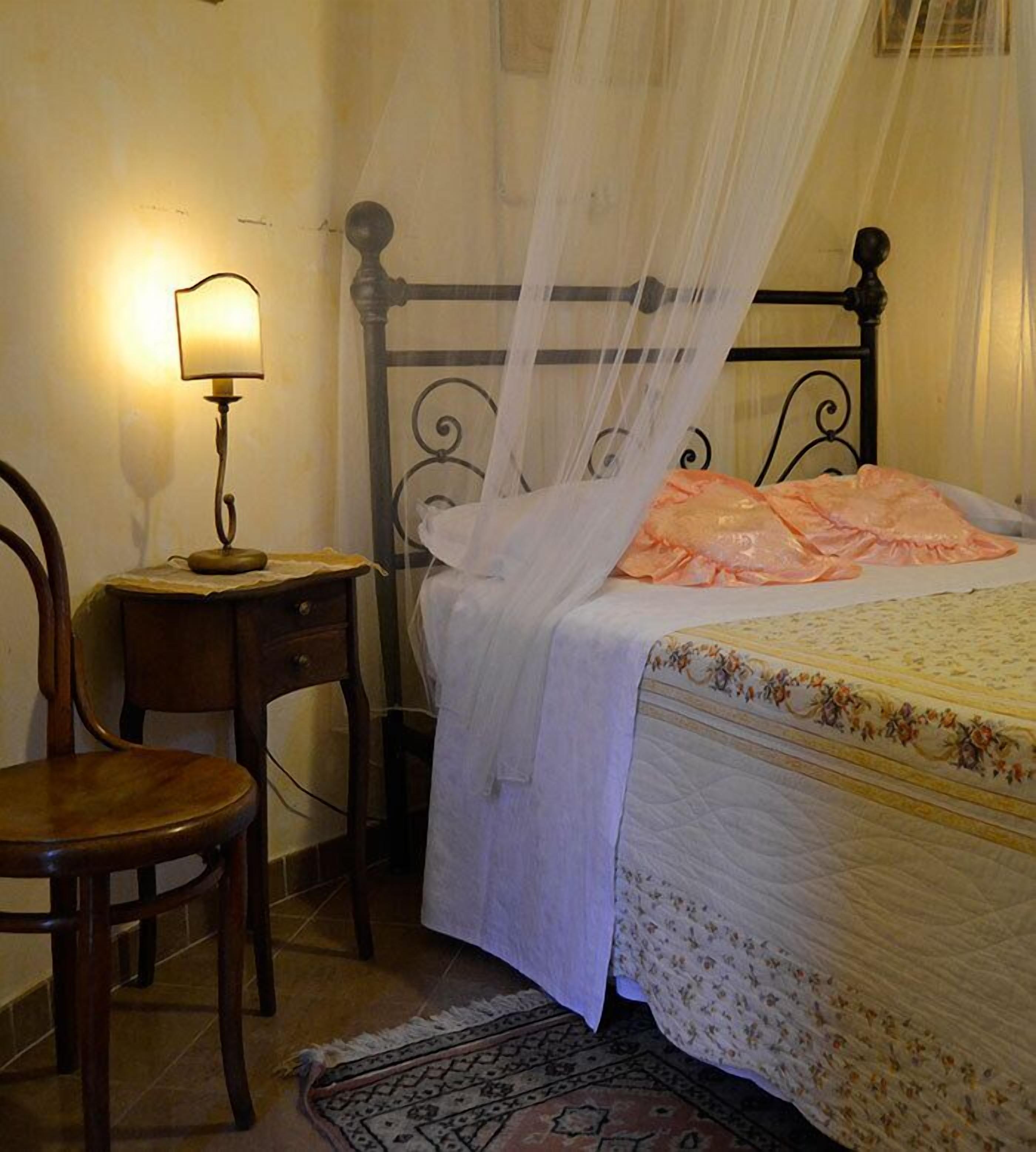 A bedroom with a bed, a nightstand, a chair, and a lamp.