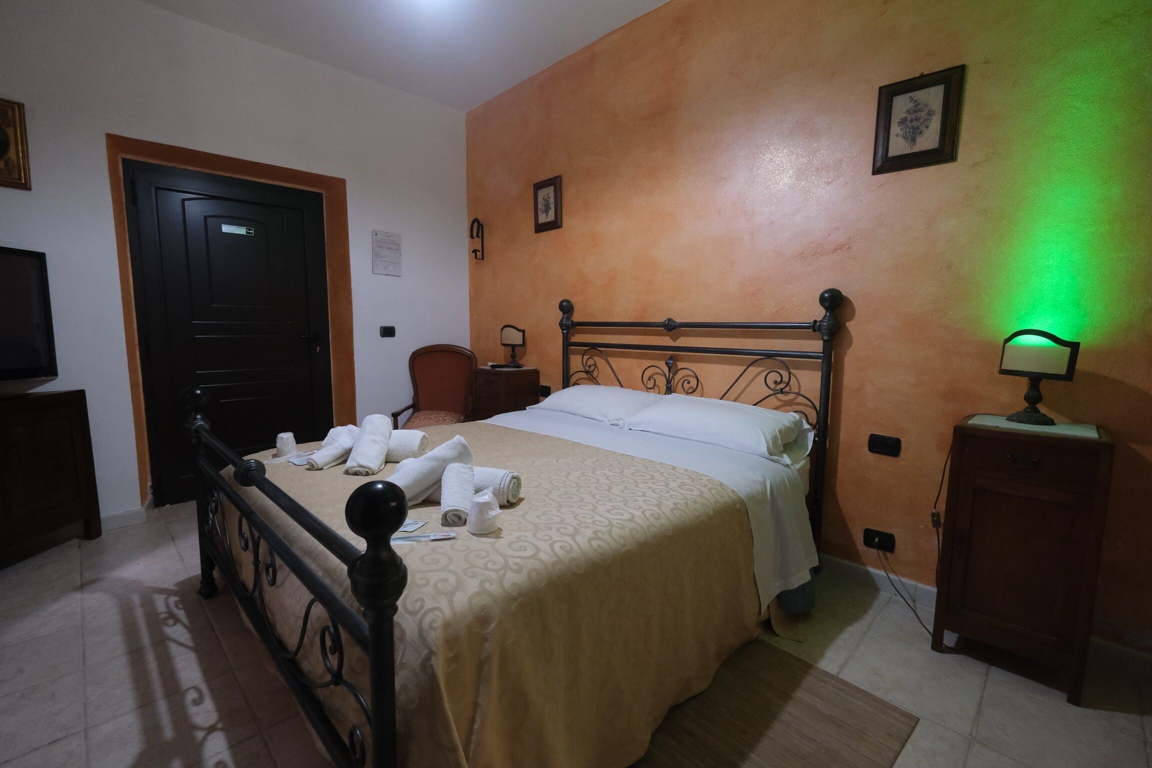 A bedroom with a bed, a nightstand, a chair, a door, and a wall-mounted light.