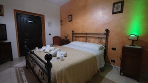 A bedroom with a bed, a nightstand, a chair, a door, and a wall-mounted light.
