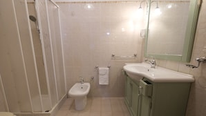 A bathroom with a shower, bidet, sink, and mirror.