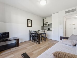 A compact room with a bed, a TV, a dining table with chairs, a kitchenette, and a door. - Charming apartment for 4 people with a balcony (Grasse)