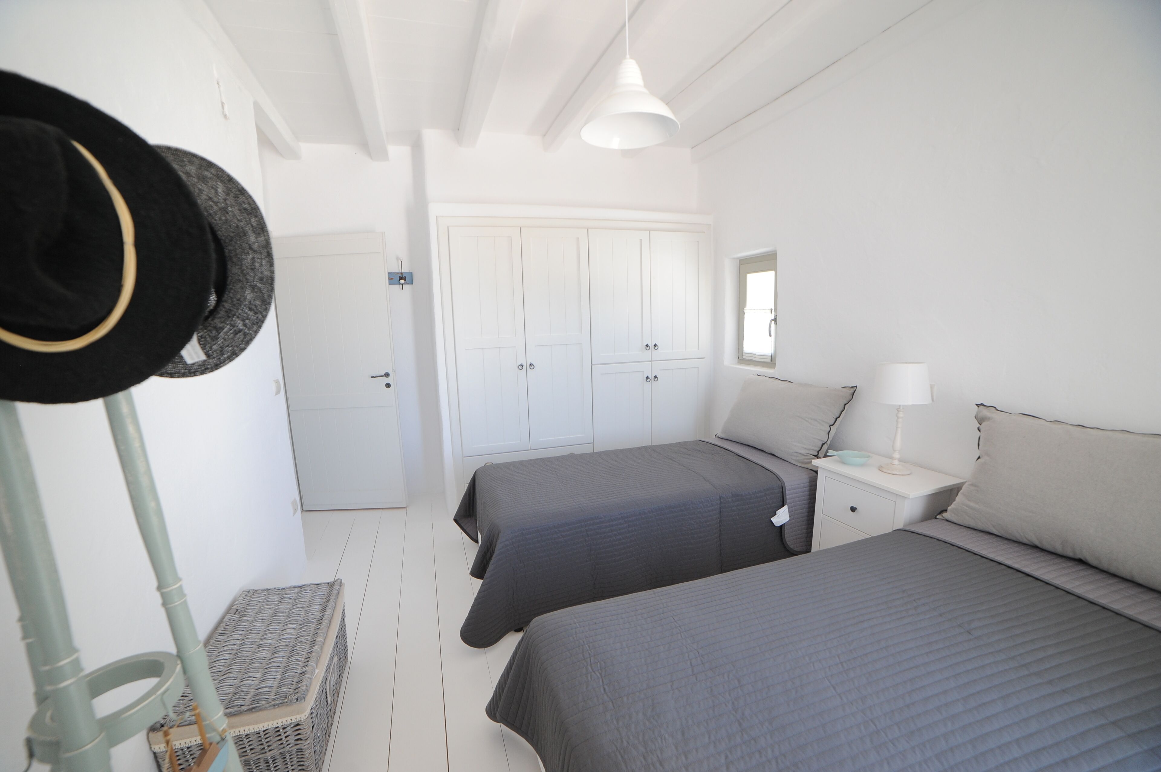 A bedroom with two beds, a wardrobe, a bedside table with a lamp, and a hat rack.