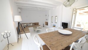 A spacious room with a wooden dining table, white chairs, a sofa, and a television. - Casa Vento - Maisonette near Santa Maria beach (SANTA MARIA)