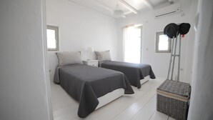 A room with two beds, a small table, a basket, and a ladder with hats. - Casa Vento - Maisonette near Santa Maria beach (SANTA MARIA)