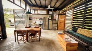 A spacious room with a dining table, chairs, a sofa, and a kitchen area with a refrigerator and cabinets.