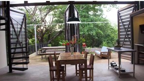 Un espace de vie à aire ouverte comprenant une table à manger en bois, des chaises, un luminaire suspendu et une vue sur la verdure à l’extérieur.