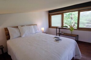 Une chambre à coucher avec un grand lit, une table de chevet, une lampe et une fenêtre donnant sur un paysage verdoyant.