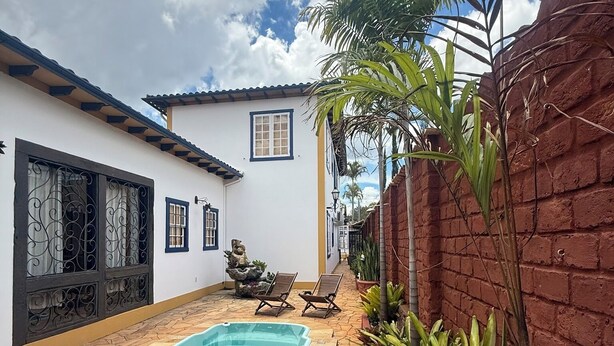 A pool area with a tiled deck, a lounge chair, and a small garden with plants. - Pousada Jardim Colonial (Tiradentes)