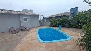 Una piscina rectangular con borde azul claro, rodeada por un patio empinado.