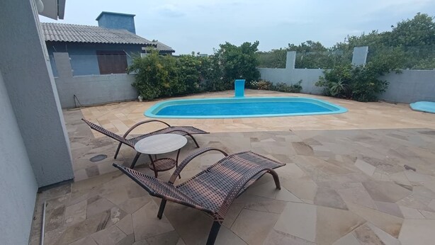 Una piscina con solárium de baldosas, dos sillas de mimbre y una mesita.