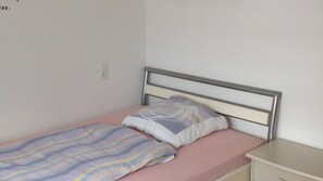 Un lit simple avec une tête de lit en métal, un matelas rose et une parure de lit à rayures.