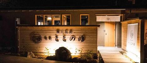 Un bâtiment à la façade en bois, une enseigne avec des caractères japonais et une entrée bien éclairée.