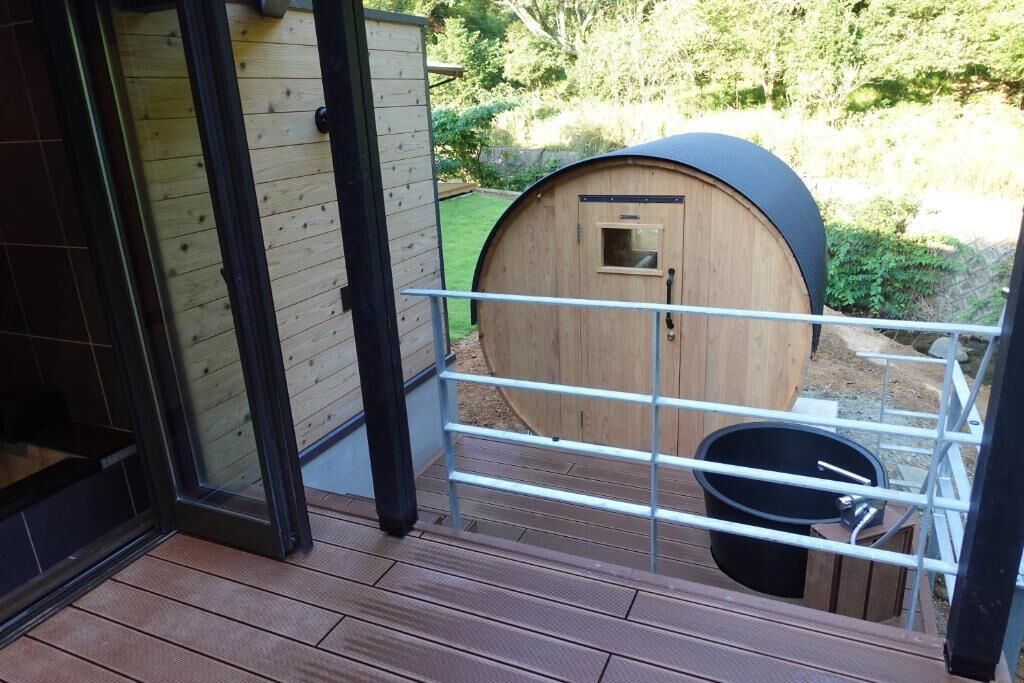 A wooden barrel structure with a metal railing, a small window, and a black bucket.