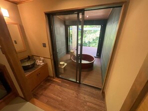 A bathroom with a wooden vanity, a sink, and a toilet. There is a glass door leading to a balcony with a hot tub. - YOKOKAWAONSEN YUDONO TOTONOYU (Shimoda)