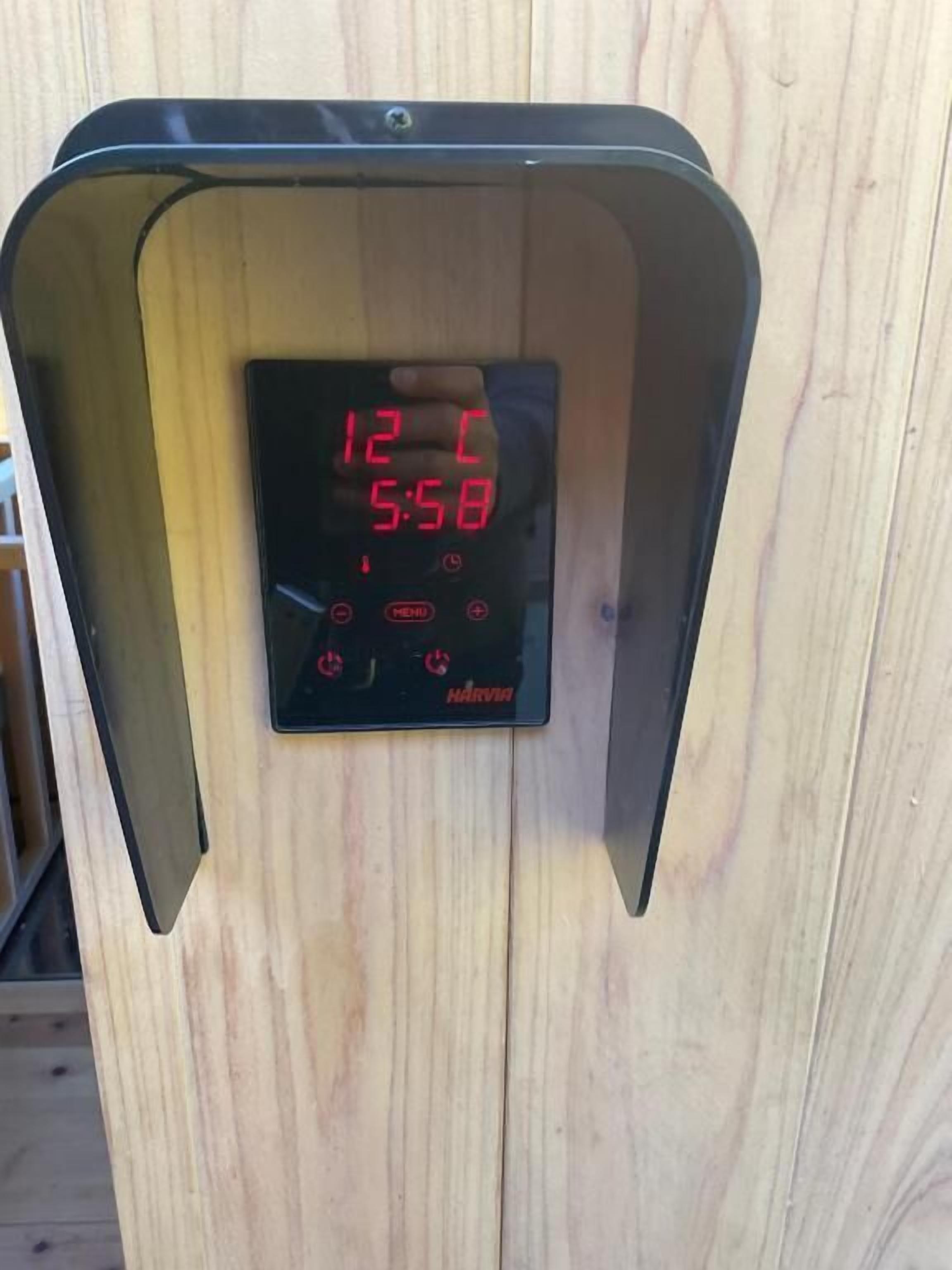 A digital clock with a red display on a black surface, mounted on a wooden wall.