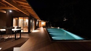 A wooden deck with a swimming pool, a dining area with tables and chairs, and a glass-enclosed room. - YOKOKAWAONSEN YUDONO TOTONOYU (Shimoda)