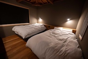 A bedroom with two beds, wooden flooring, a window with blinds, and wall-mounted lighting. - YOKOKAWAONSEN YUDONO TOTONOYU (Shimoda)