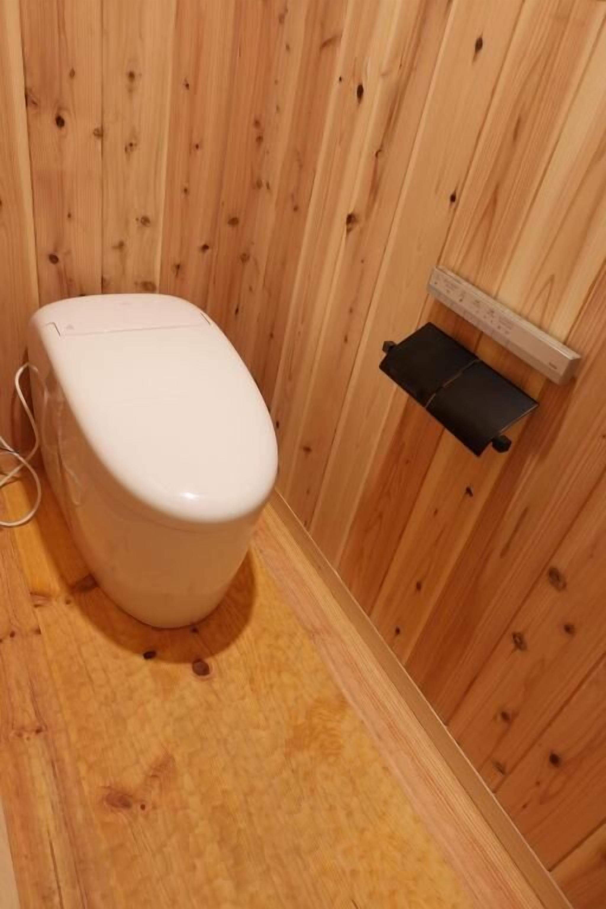 A wooden-paneled bathroom with a white toilet and a small shelf.