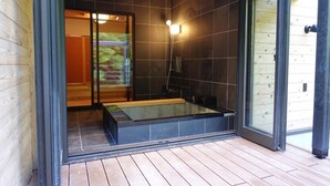 A modern bathroom with a glass-enclosed bathtub, dark tiled walls, and a wooden deck outside. - YOKOKAWAONSEN YUDONO TOTONOYU (Shimoda)