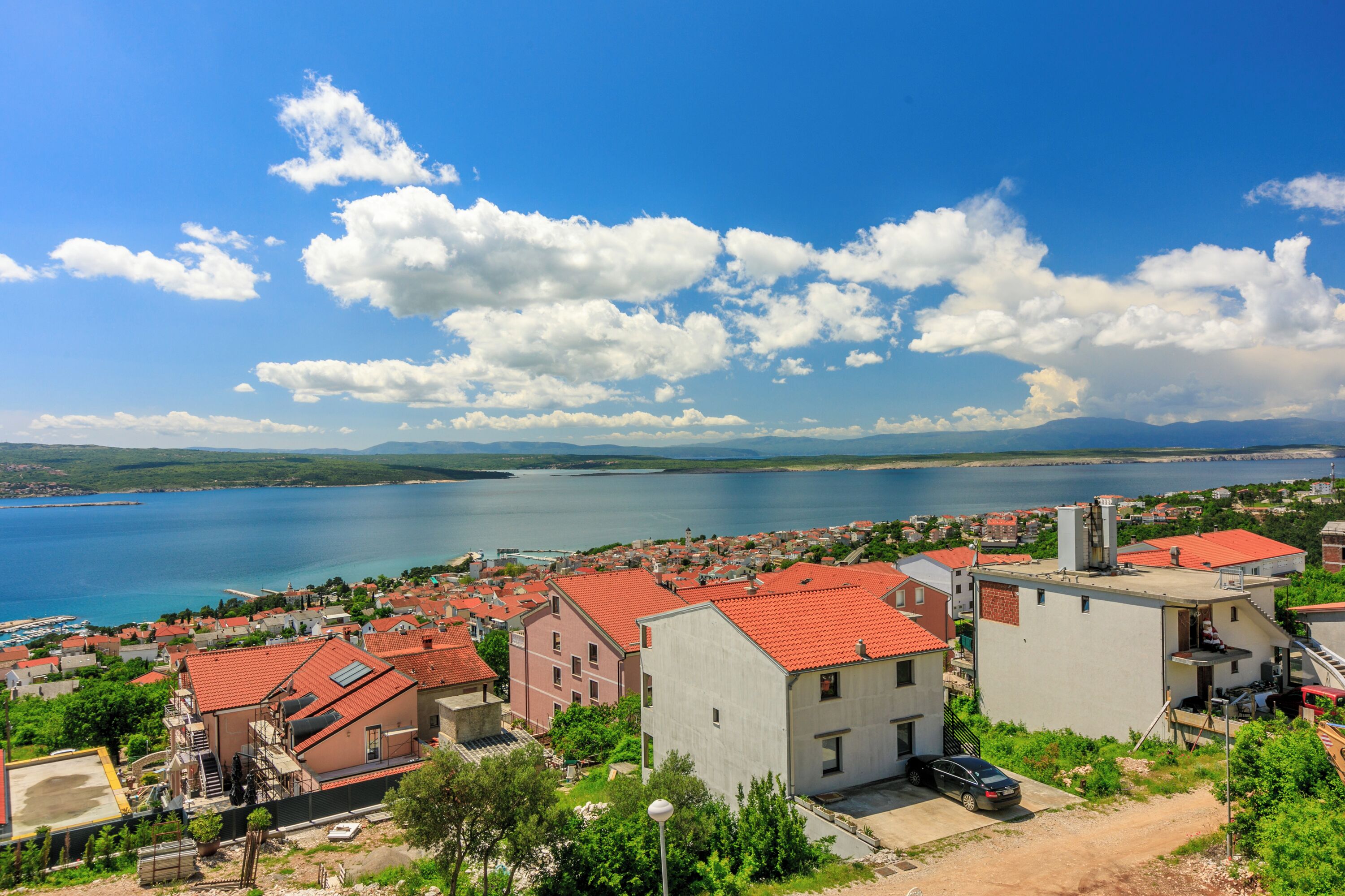 Uma vila costeira com edifícios de telhados vermelhos, céu azul límpido e vista para o mar.