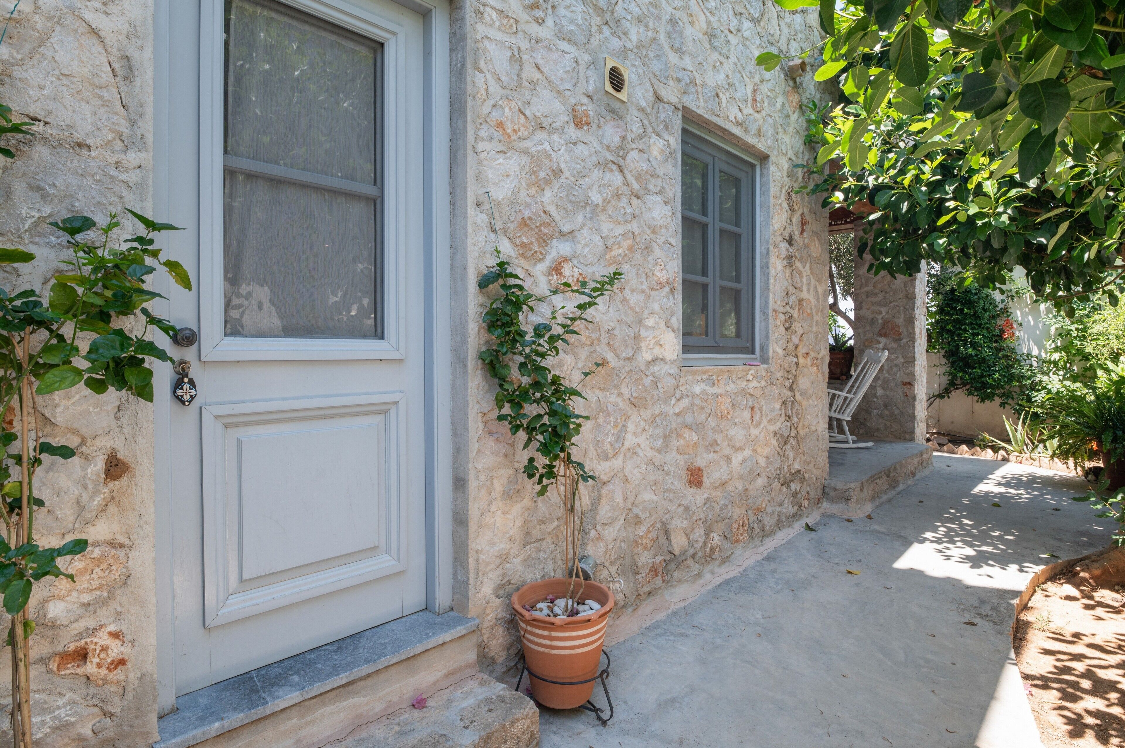 Un bâtiment en pierre avec une porte et des fenêtres blanches, un pot de fleurs et un escalier.