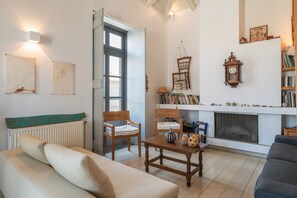 Un salon comprenant un canapé, des fauteuils, une table basse, une cheminée, des étagères et des horloges murales.