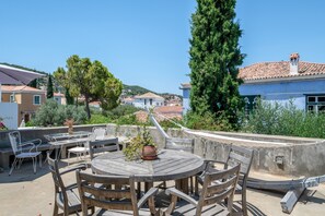 Une terrasse extérieure avec une table ronde en bois et des chaises, entourée de verdure et donnant sur un quartier résidentiel.