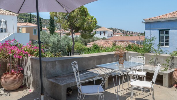 Una terraza con mobiliario exterior, un paraguas grande y vistas de los edificios y el paisaje circundante.