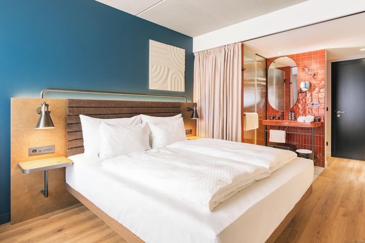 Una camera d'albergo moderna con un letto, comodini, uno specchio e un bagno con un lavandino e specchio.