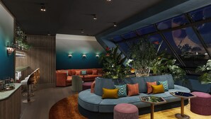 A modern lounge area with a curved sofa, a round coffee table, and a bar area with stools. - Hotel Schani Naschmarkt (Vienna)