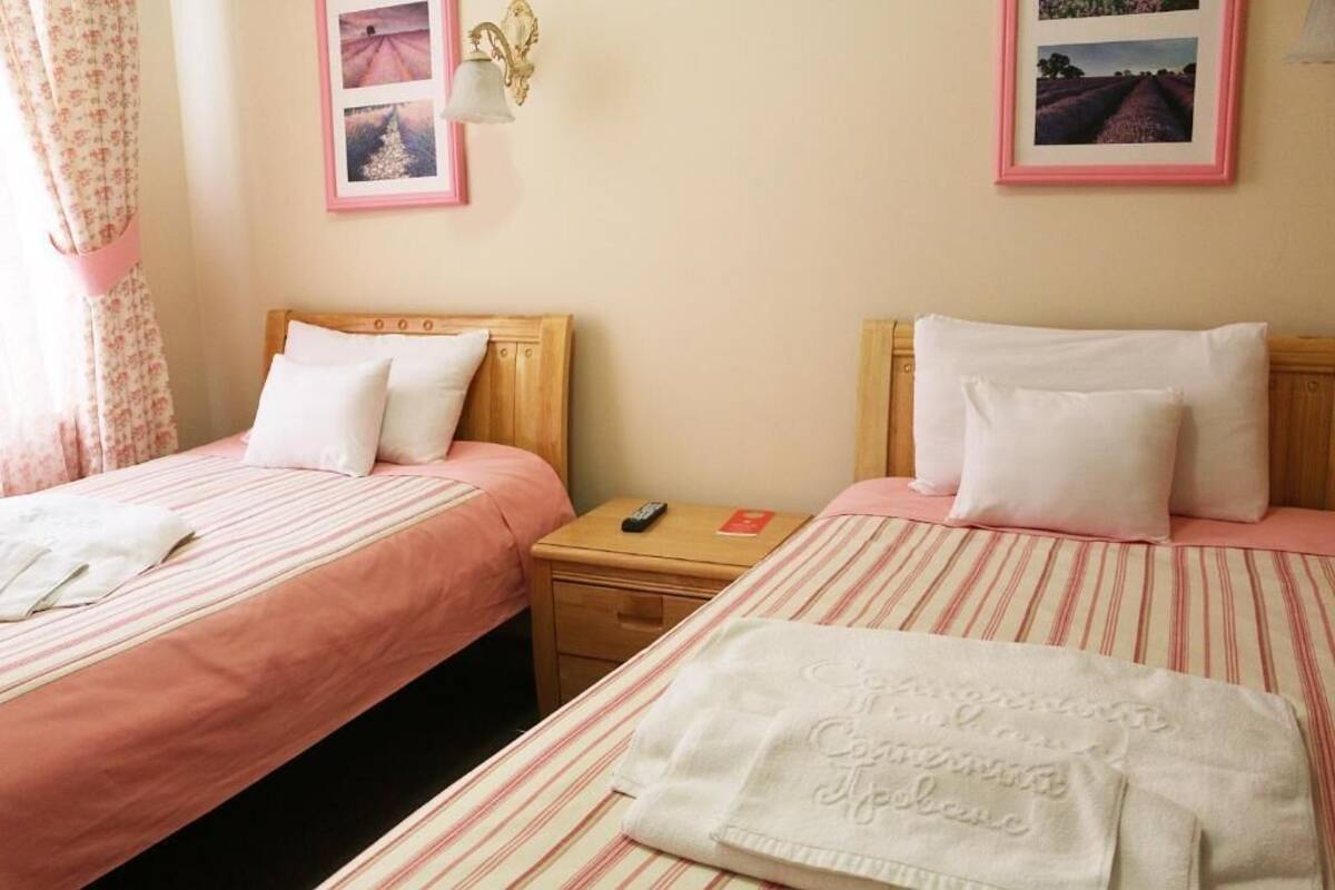 Una habitación de hotel con dos camas individuales, una mesita de noche con control remoto y una lámpara de pared.