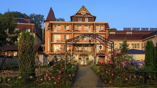 A hotel with a central entrance, a sign above the entrance, and a garden with flowers.