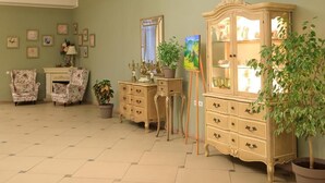 A room with a green wall, floral armchairs, a cream-colored cabinet, and a potted plant.