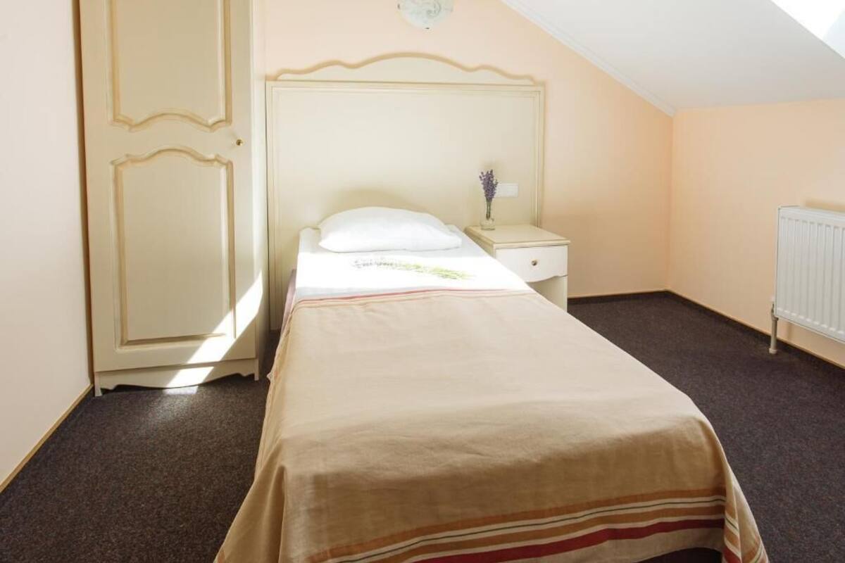 Una cama individual con cabecera, una mesita de noche con lámpara y un radiador.