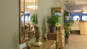 A room with a large ornate mirror, a wooden dresser, and potted plants.