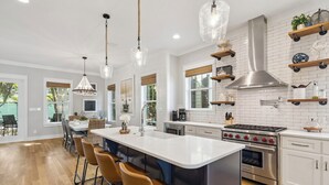 Uma cozinha moderna com ilha central, banquetas, eletrodomésticos de aço inoxidável e iluminação pendente.